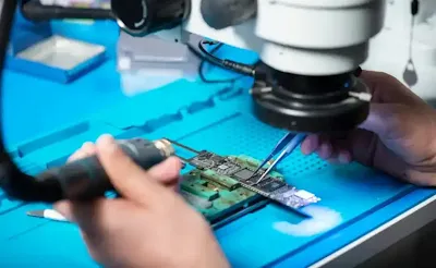 Technician repairing avionic PCB using leaded solder under microscope