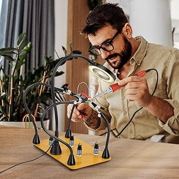 A hobbyist using a temperature-controlled soldering station with magnifying lamp