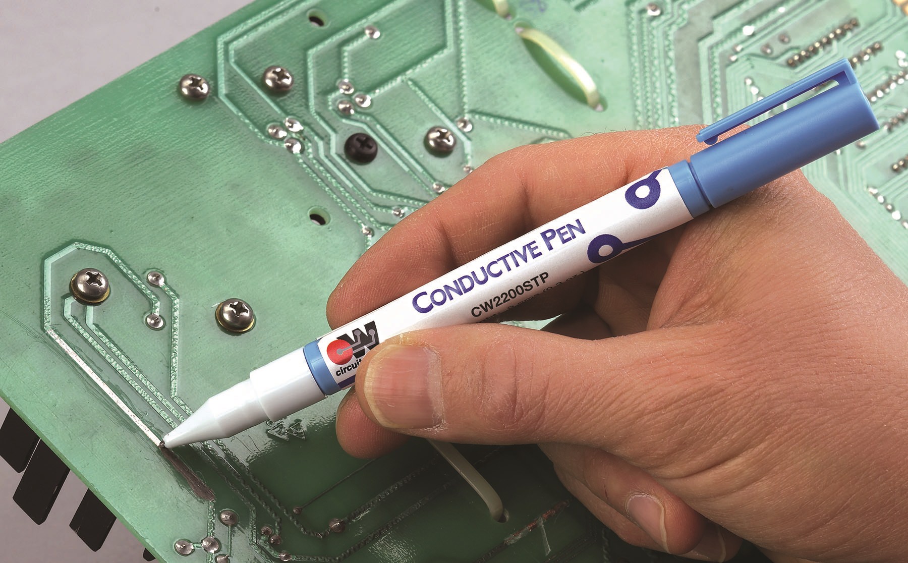 Hobbyist repairing a broken trace on a PCB with a conductive pen