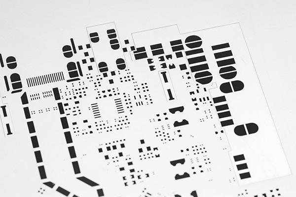 Close-up of an SMT stencil showing precision-cut apertures for various components and alignment fiducial marks