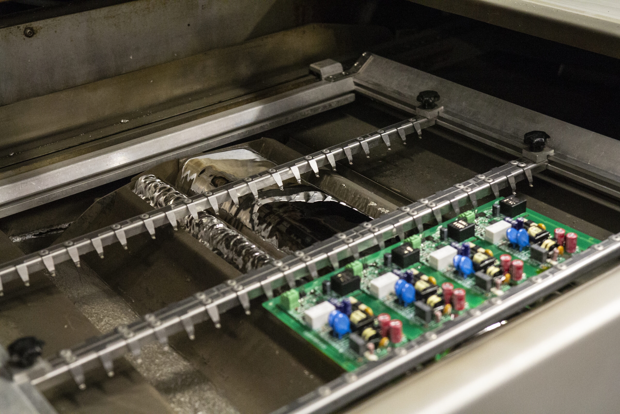 A wave soldering machine with conveyor and solder pot in operation