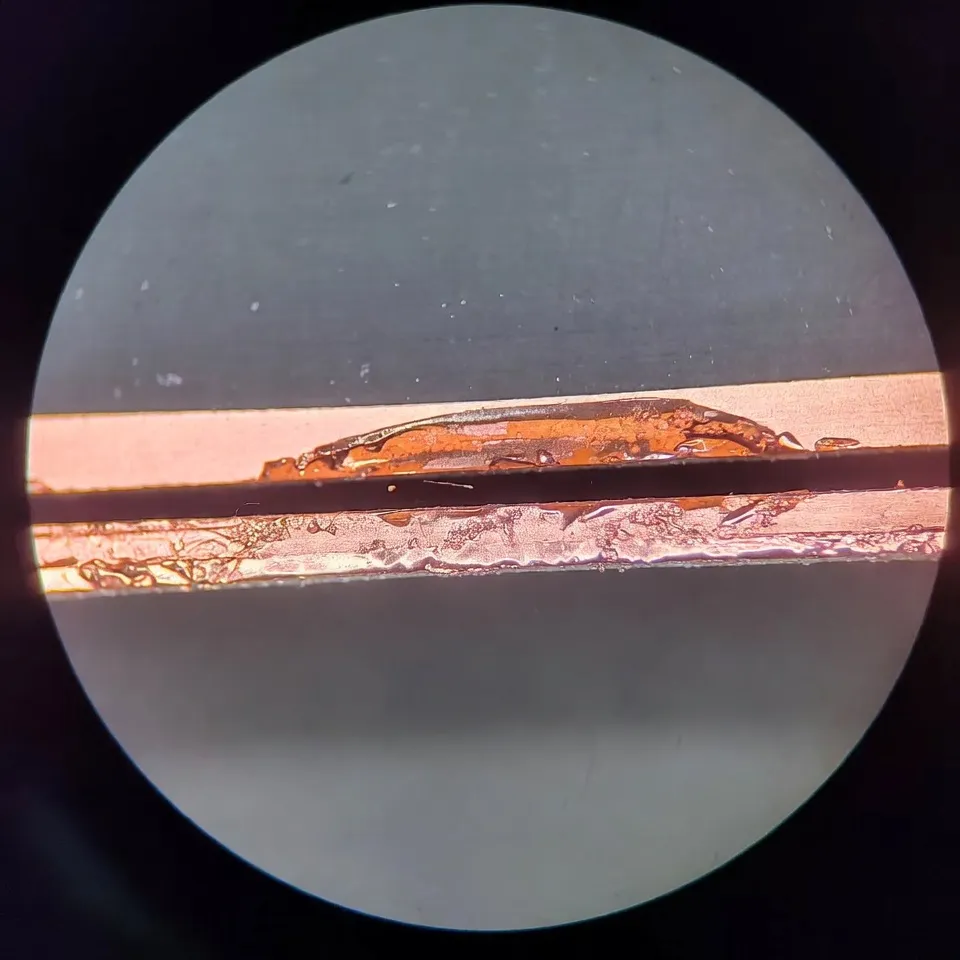 Microscope view of laser-cut FPC edge with trace too close &mdash; showing copper smear, edge roughness, and potential short path