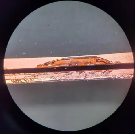 Microscope view of laser-cut FPC edge with trace too close — showing copper smear, edge roughness, and potential short path