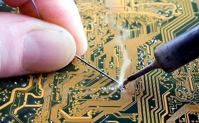 Close up of a soldering iron heating a PCB pad for component attachment